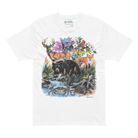 A white short-sleeve crewneck t-shirt featuring a colorful front graphic print of a deer, bear, fox, and crab in a natural setting with flowers and a cabin. The words 'with wildflowers' are printed in white script across the center of the graphic.