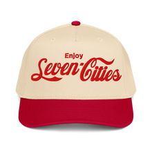 A structured baseball cap with a cream-colored crown and a red curved brim. The front of the cap features the text 'Enjoy Seven Cities' embroidered in red, styled like the Coca-Cola script.