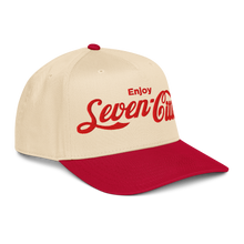 A structured baseball cap with a cream-colored crown and a red curved brim. The front of the cap features the text 'Enjoy Seven Cities' embroidered in red, styled like the Coca-Cola script.

