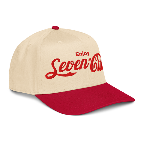 A structured baseball cap with a cream-colored crown and a red curved brim. The front of the cap features the text 'Enjoy Seven Cities' embroidered in red, styled like the Coca-Cola script.

